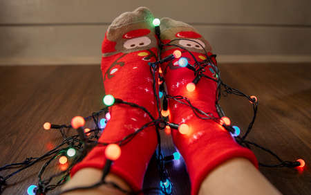 Legs at red christmas socks with colorful garlands on wooden backgroundの写真素材