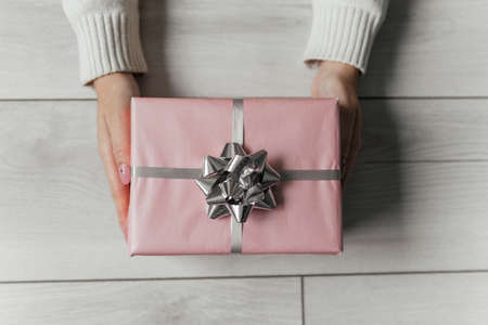 Hands hold pink christmas present on gray isolated background