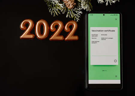 Phone with electronic Vaccination Certificate on black Christmas background and number 2022の写真素材