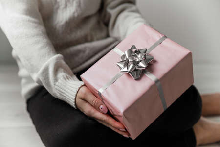 Woman in a white sweater sitting on floor and holding a pink gift in her hands on a gray backgroundの写真素材