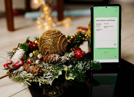 Phone with electronic Covid Vaccination Certificate on light Christmas background