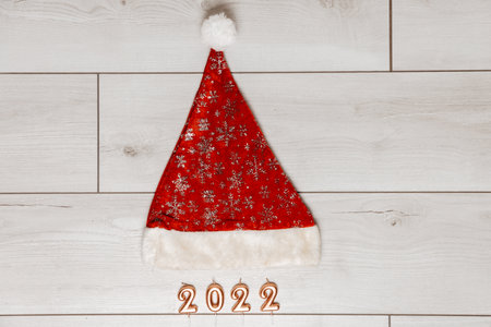 Festive Christmas and new year card with red santa hat and number 2022 on gray wooden background