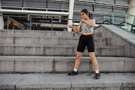 Teenage girl doing sports warm-up and wrestling exercises on the street against the city backgroundの写真素材