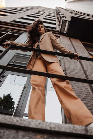 Tall stylish girl with oversized jacket posing near the railing and steps on the city backgroundの写真素材