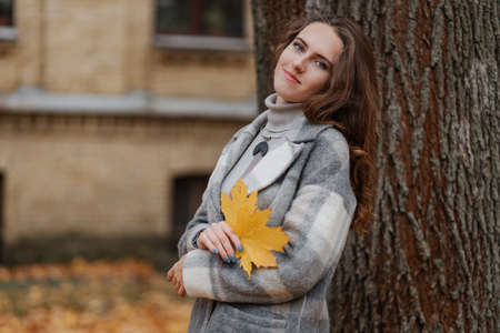 Young smiling girl in a gray coat holds a yellow leaf in her handsの写真素材