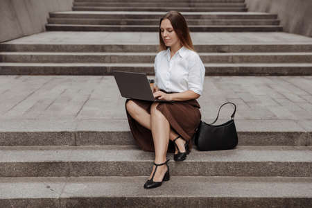 Young business woman sitting on a stairs with a laptop of the modern office building backgroundの写真素材