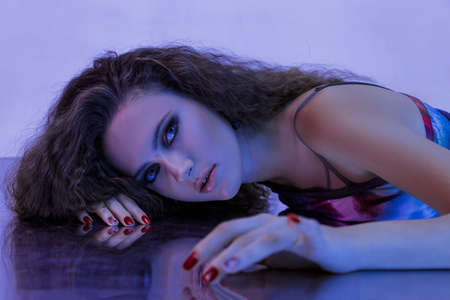 Portrait of a beautiful young woman with long curly hair in neon lightの写真素材