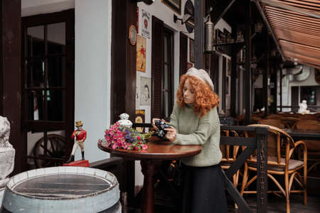 A woman in a beret and a green sweater holds a camera in her hands and takes shootsの写真素材