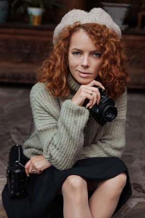A woman in a beret and a green sweater holds a camera in her hands and takes shootsの写真素材