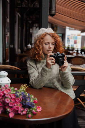 A woman in a beret and a green sweater holds a camera in her hands and takes shootsの写真素材