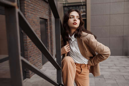 Tall stylish girl with oversized jacket posing near the railing and steps on the city backgroundの写真素材