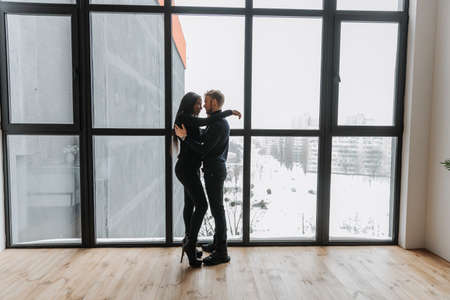 Couple in love tenderly hugs in a cozy home environment and panorama windowの写真素材