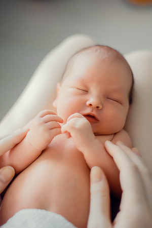 A newborn baby lies on the mother's lap. Mother holds her newborn baby. Woman relaxing in a white bedroom. Family at homeの写真素材