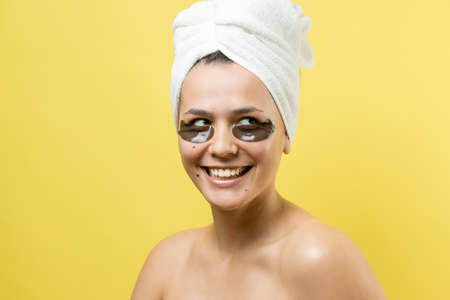 Young beautiful girl in a white towel on his head wears collagen gel patches under her eyes. Mask under eyes treatment face.の写真素材