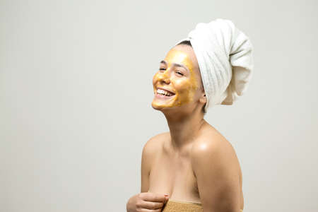 Beauty portrait of woman in white towel on head with gold nourishing mask on face. Skincare...