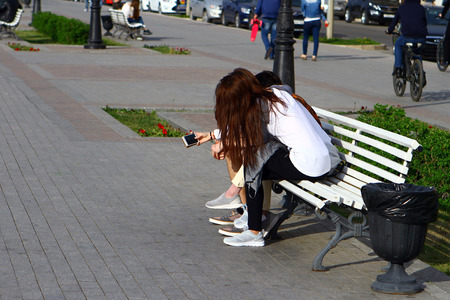 Girls teenagers are having fun with smart phone on a benchの写真素材