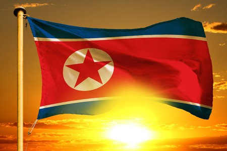Democratic Peoples Republic of Korea (North Korea) flag weaving on the beautiful orange sunset backgroundの写真素材