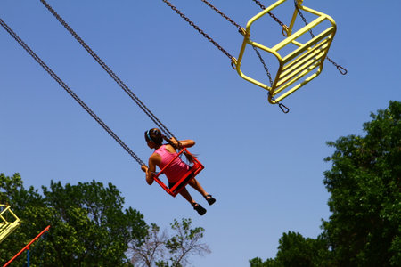Girl on chain carousel in park against blue sky, photo of people