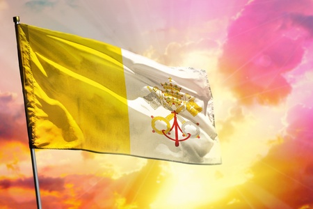 Fluttering Holy See flag on beautiful colorful sunset or sunrise background. Holy See success and happiness concept.の写真素材