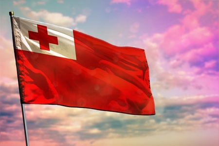 Fluttering Tonga flag on colorful cloudy sky background. Tonga prospering concept.の写真素材