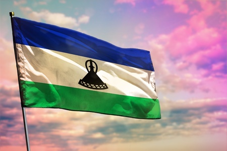Fluttering Lesotho flag on colorful cloudy sky background. Lesotho prospering concept.