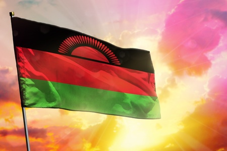 Fluttering Malawi flag on beautiful colorful sunset or sunrise background. Malawi success and happiness concept.の写真素材