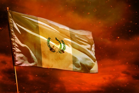 Fluttering Guatemala flag on crimson red sky with smoke pillars background. Guatemala problems concept.の写真素材