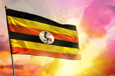 Fluttering Uganda flag on beautiful colorful sunset or sunrise background. Uganda success and happiness concept.の写真素材