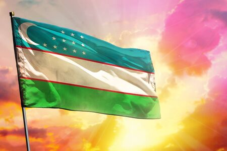 Fluttering Uzbekistan flag on beautiful colorful sunset or sunrise background. Uzbekistan success and happiness concept.の写真素材