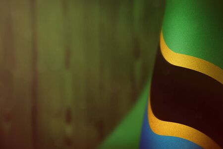 Tanzania hanging flag for honour of veterans day or memorial day on green blurred natural wood wall background. Tanzania glory to the heroes of war concept.の写真素材