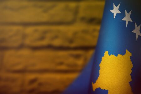 Kosovo hanging flag for honour of veterans day or memorial day on orange blurred painted brick wall background. Kosovo glory to the heroes of war concept.の写真素材