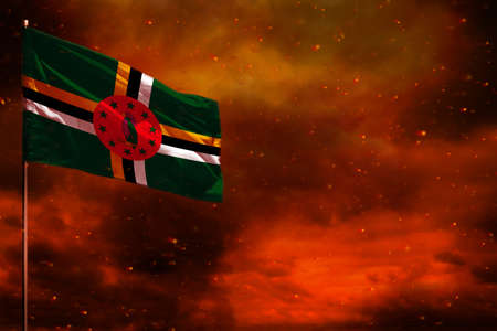 Fluttering Dominica flag mockup with blank space for your data on crimson red sky with smoke pillars...