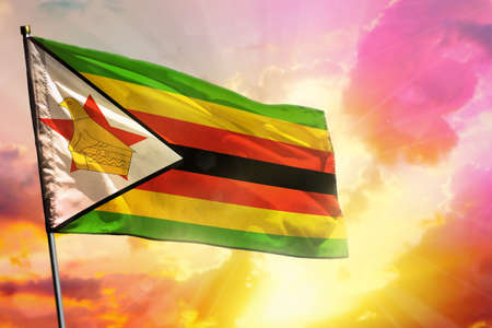Fluttering Zimbabwe flag on beautiful colorful sunset or sunrise background. Zimbabwe success and happiness concept.の写真素材