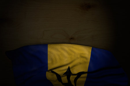 beautiful dark photo of Barbados flag with large folds on dark wood with empty space for your text - any occasion flag 3d illustrationの写真素材