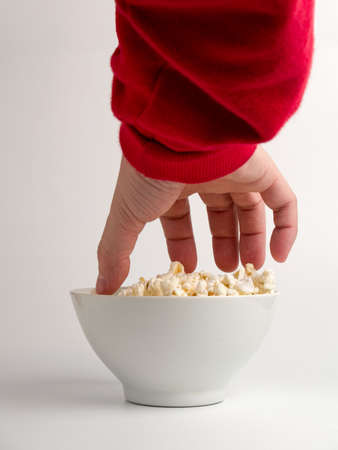 A hand trying to reach some popcorns from a bowl.の写真素材