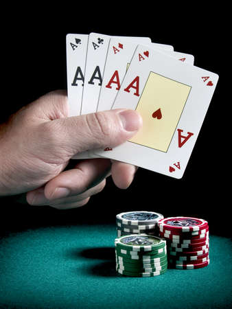 A man's hand holding four aces over three piles of differents colors chips on a green felt.