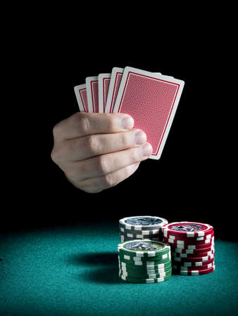 A man's hand holding four cards over three piles of differents colors chips on a green felt.のeditorial素材