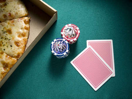 Two cards, two piles of chips and a box of pizza over a green felt.のeditorial素材
