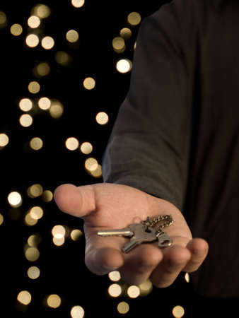A man holding a pair of keys on his hand over a blurred lights background.の写真素材