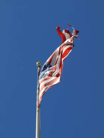 A ripped american flag waving over a blue sky.の写真素材