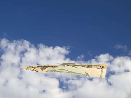 A ten dollars bill airplane flying over the clouds on a blue sky.の写真素材