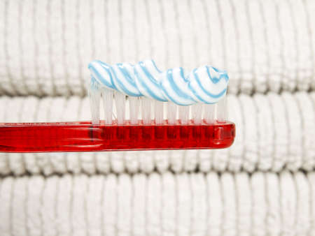A red toothbrush full of toothpaste with white towels as background.の写真素材