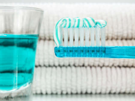 A blue toothbrush with toothpaste, a glass full of mouthwash and towels on the background.の写真素材