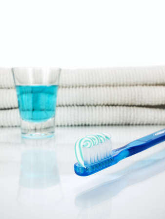 A blue toothbrush with toothpaste, a glass full of mouthwash and towels on the background.の写真素材