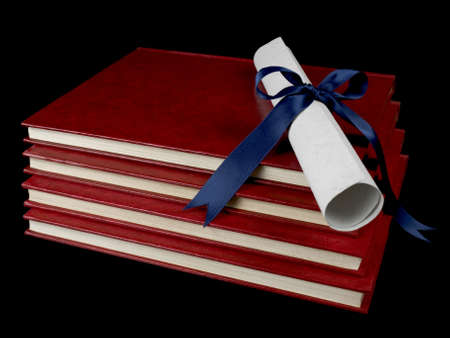 A diploma with blue ribbon over several books. Isolated on black.の写真素材