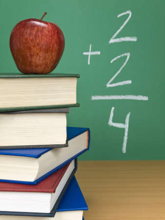 An addition on the chalkboard with an apple on top of a pile of books.