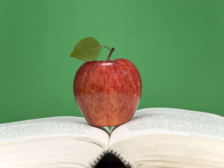 A red apple over an open book. Blank chalkboard on the background.の写真素材