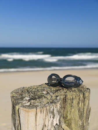 A pair of goggles sitting over a log in the beach.の写真素材