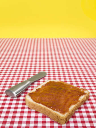 A slice of bread spread with jam and a knife over the table.の写真素材