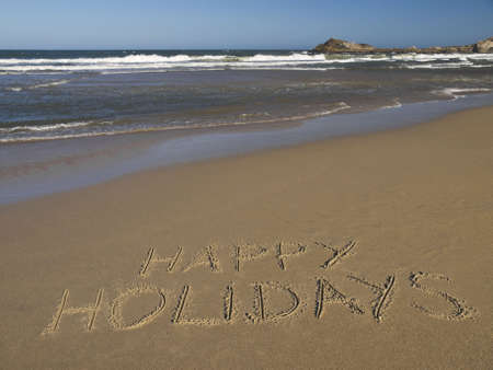 Happy holidays written on the sand beside the ocean.の写真素材